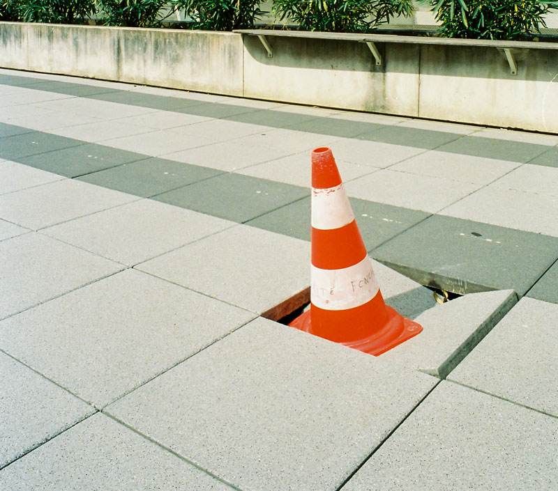 A cone that is covering a cracked pavement.